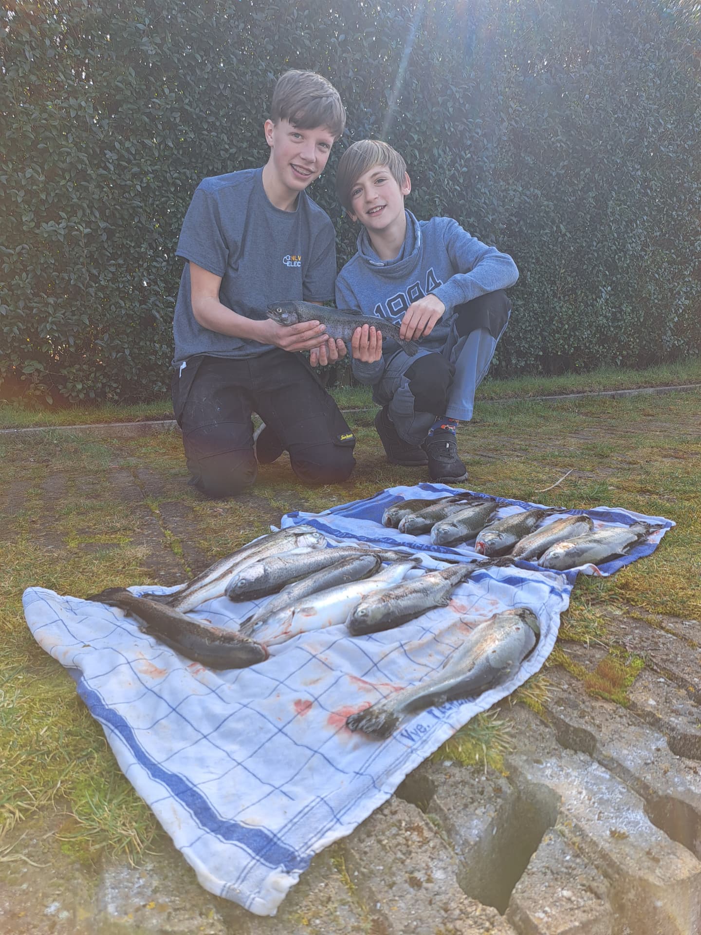 Twee jongens knielen trots bij hun forelvangst op een handdoek